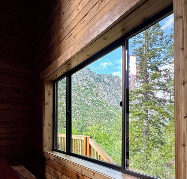 Une cabane dotée d’une grande fenêtre donnant sur un paysage de montagne et de forêt.