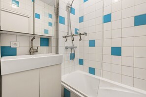 A bathroom with a white sink, a mirror, a shower with a handheld showerhead, and a bathtub.