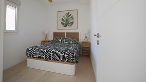 Ett sovrum med en säng, en takfläkt, ett nattduksbord med en lampa och en inramad växt på väggen.