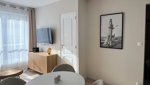 Een moderne kamer met een ronde tafel, vier stoelen, een plafondventilator, een flatscreen televisie, een inlijsting foto aan de muur, en een raam met dunne gordijnen.