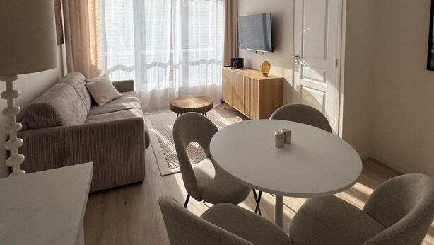 Een moderne woonkamer met een bank, een eettafel met stoelen, een televisie en een plafondventilator.