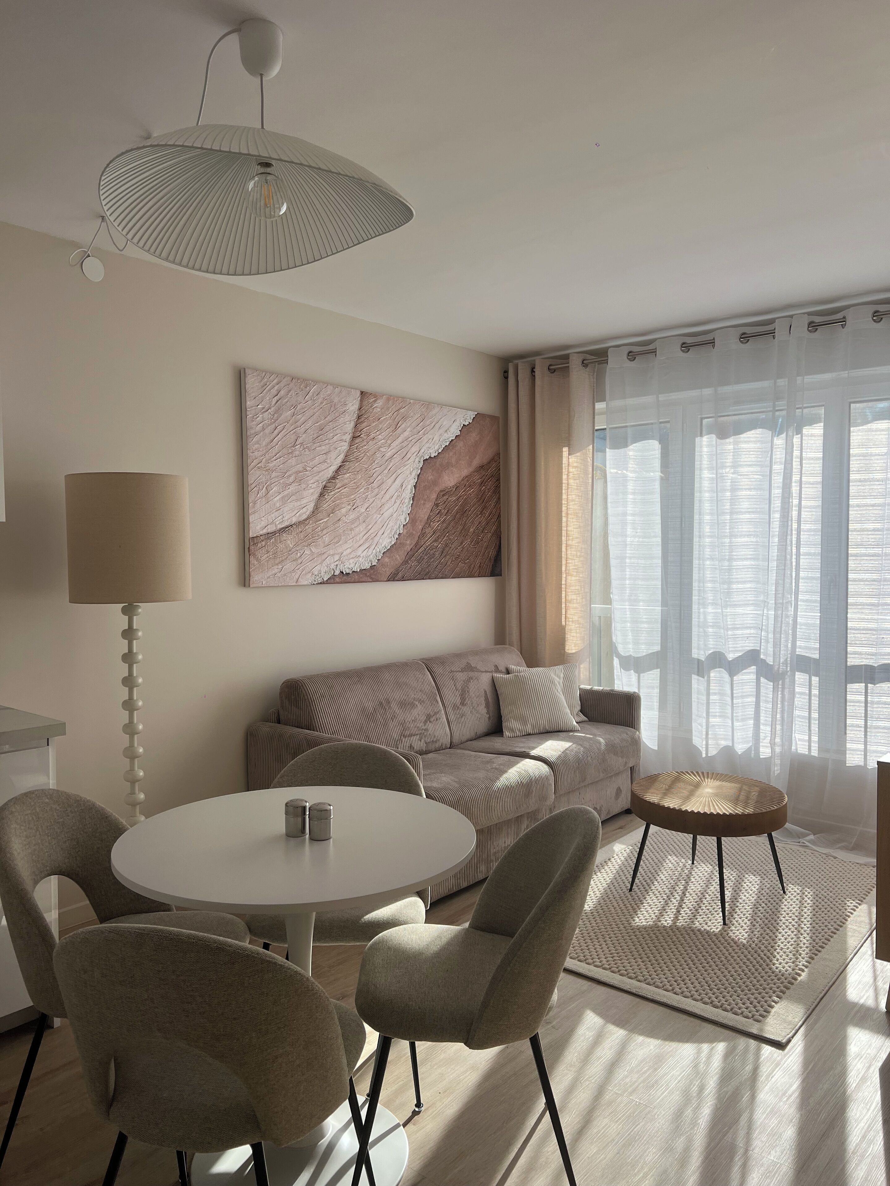 Una sala de estar moderna con una mesa de comedor redonda, un sofá beige y un cuadro abstracto grande en la pared.