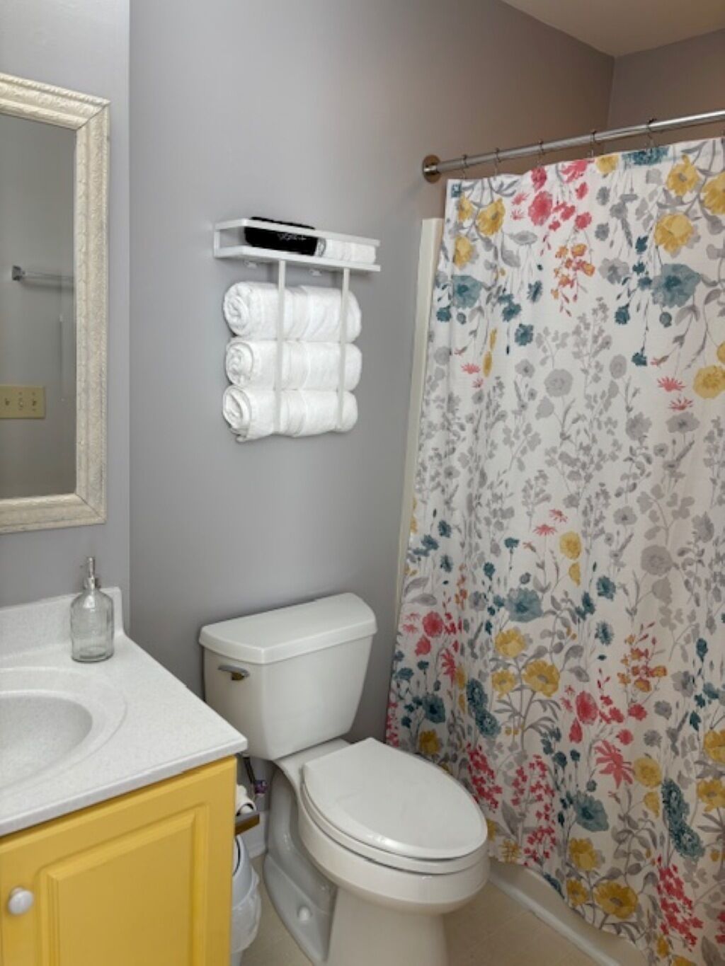 A bathroom with a toilet, a sink, a mirror, and a shower curtain with a floral pattern.