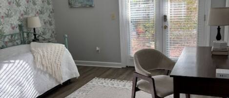A bedroom with a bed, a chair, a table, a ceiling fan, and a window with blinds.