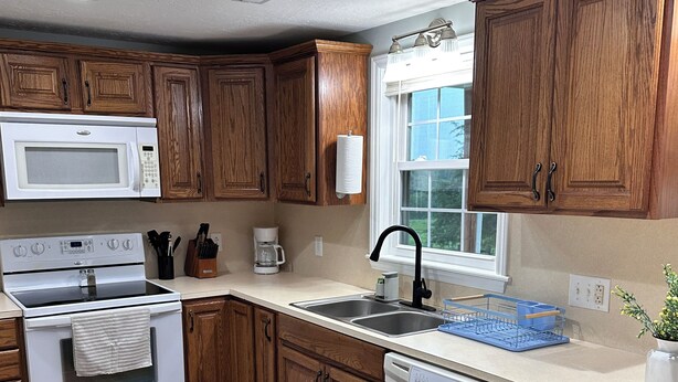 A kitchen with wooden cabinets, a white microwave, an oven, a sink, and a dishwasher.