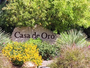A sign reading "Casa de Oro" surrounded by lush greenery and yellow flowers.