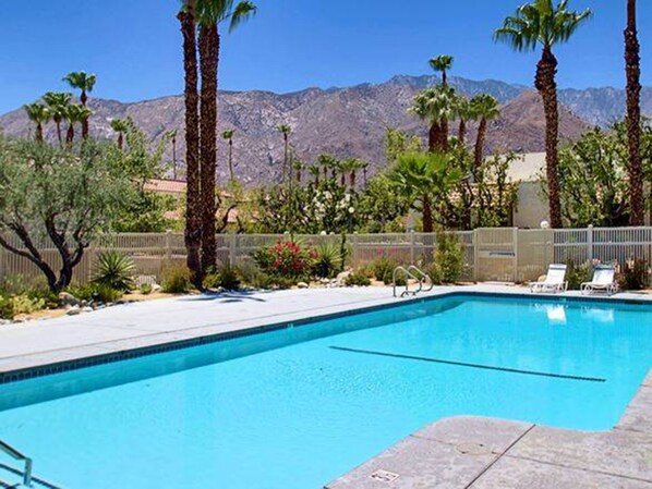 A swimming pool with a clear blue water, surrounded by palm trees and a mountain backdrop.