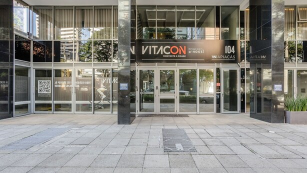 Entrada de um edifício moderno com portas de vidro, uma placa com o dizer 