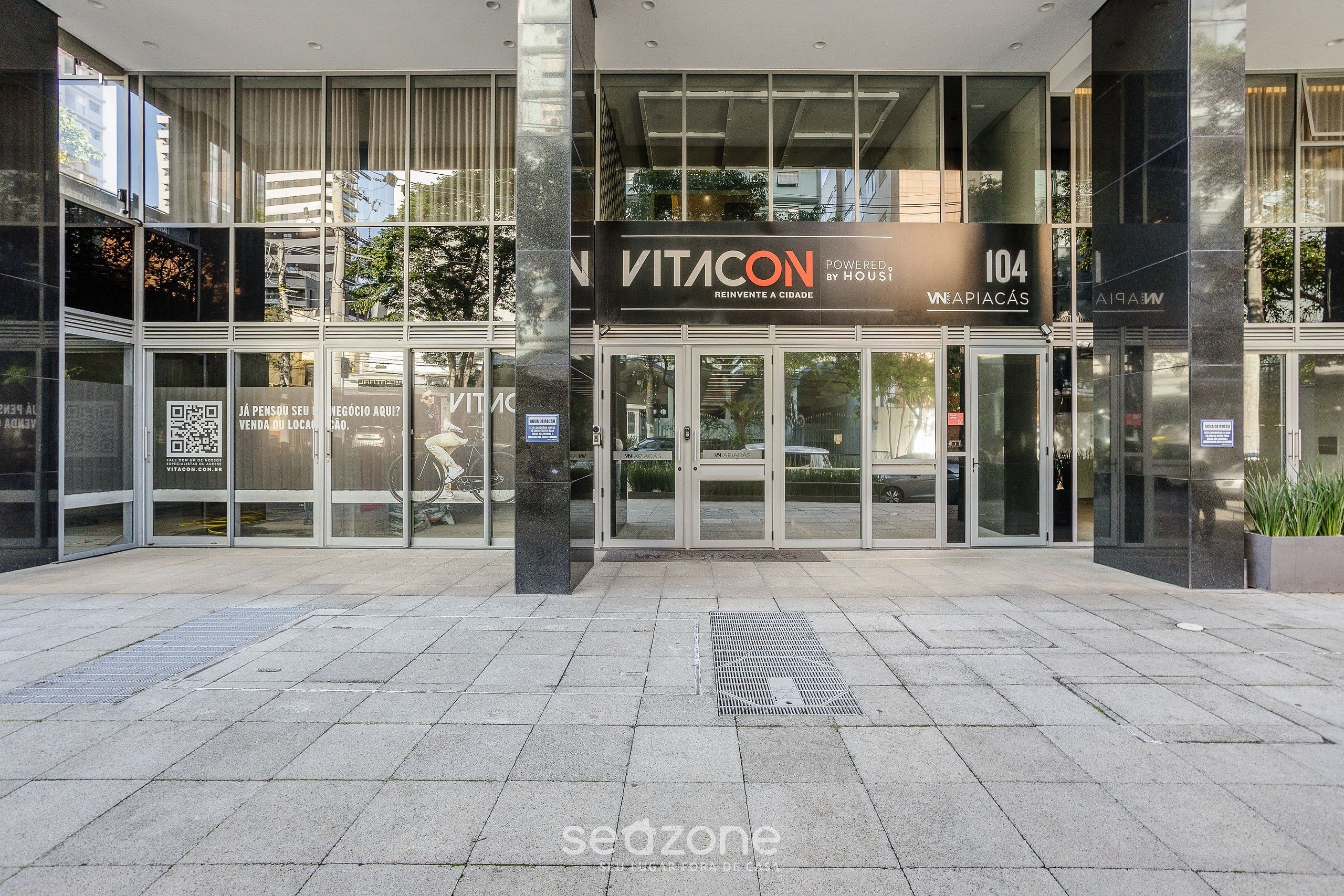 Une entrée moderne avec des portes en verre, une enseigne indiquant « VITACON 104 » et un code QR sur le verre.