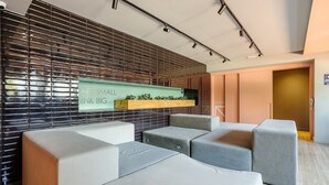 Uma área de espera moderna com parede de treliça de metal, uma placa com a inscrição 'ART SMALL THINK BIG' e um pequeno aparador de plantas.
