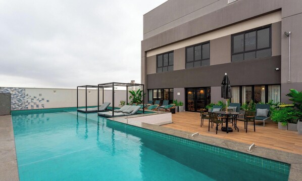 A rooftop pool with lounge chairs, a covered seating area, and a building with large windows and a door. - Beautiful Units at Viva Benx Vila Olimpia - VBX (São Paulo)