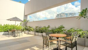 Une terrasse extérieure avec des tables et des chaises, entourée de jardinières et offrant une vue sur un bâtiment moderne.