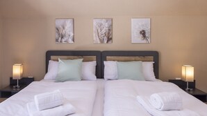 Una cama doble con dos almohadas, una mesita de noche con lámpara y tres cuadros colgados en la pared.