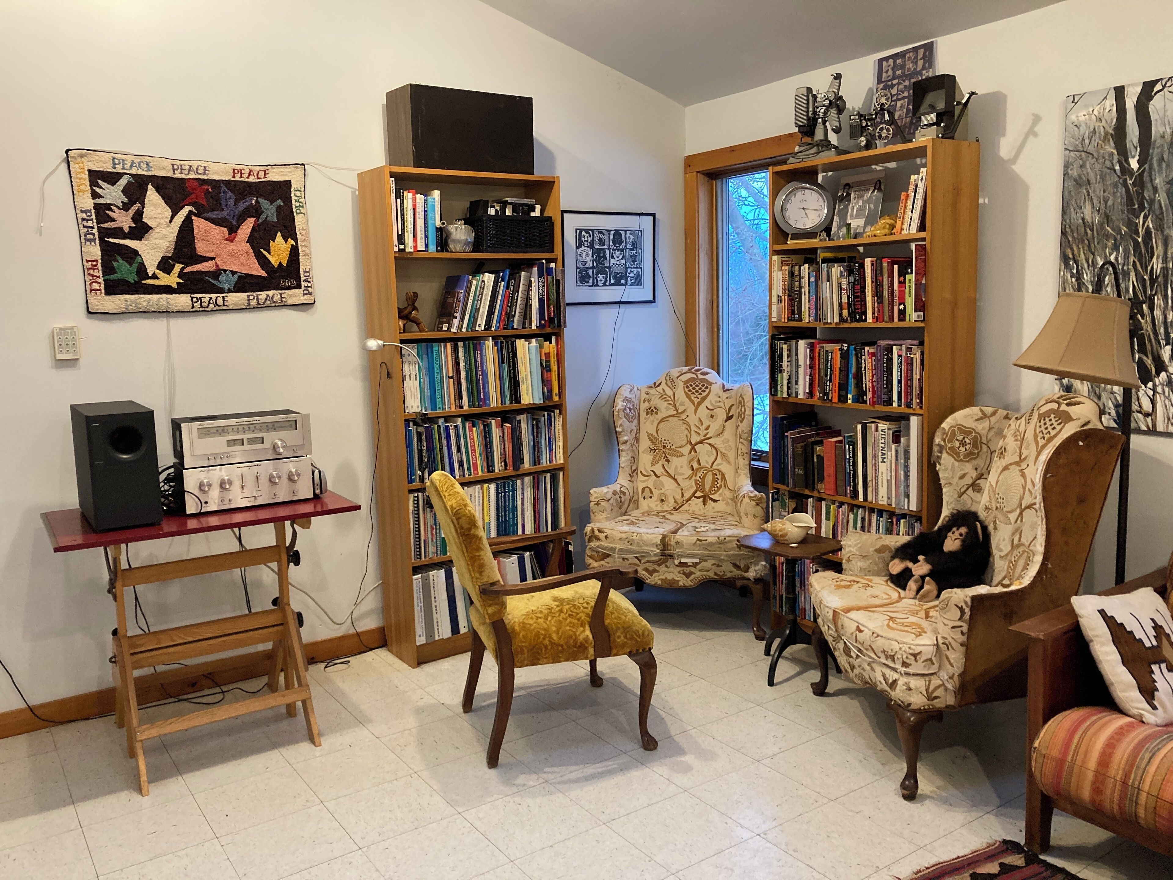 A cozy living room with a bookshelf, a vintage radio, a yellow armchair, and a plush armchair with a stuffed animal.