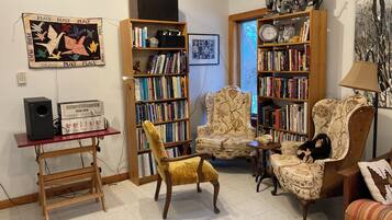 A cozy living room with a bookshelf, a vintage radio, a yellow armchair, and a plush armchair with a stuffed animal.