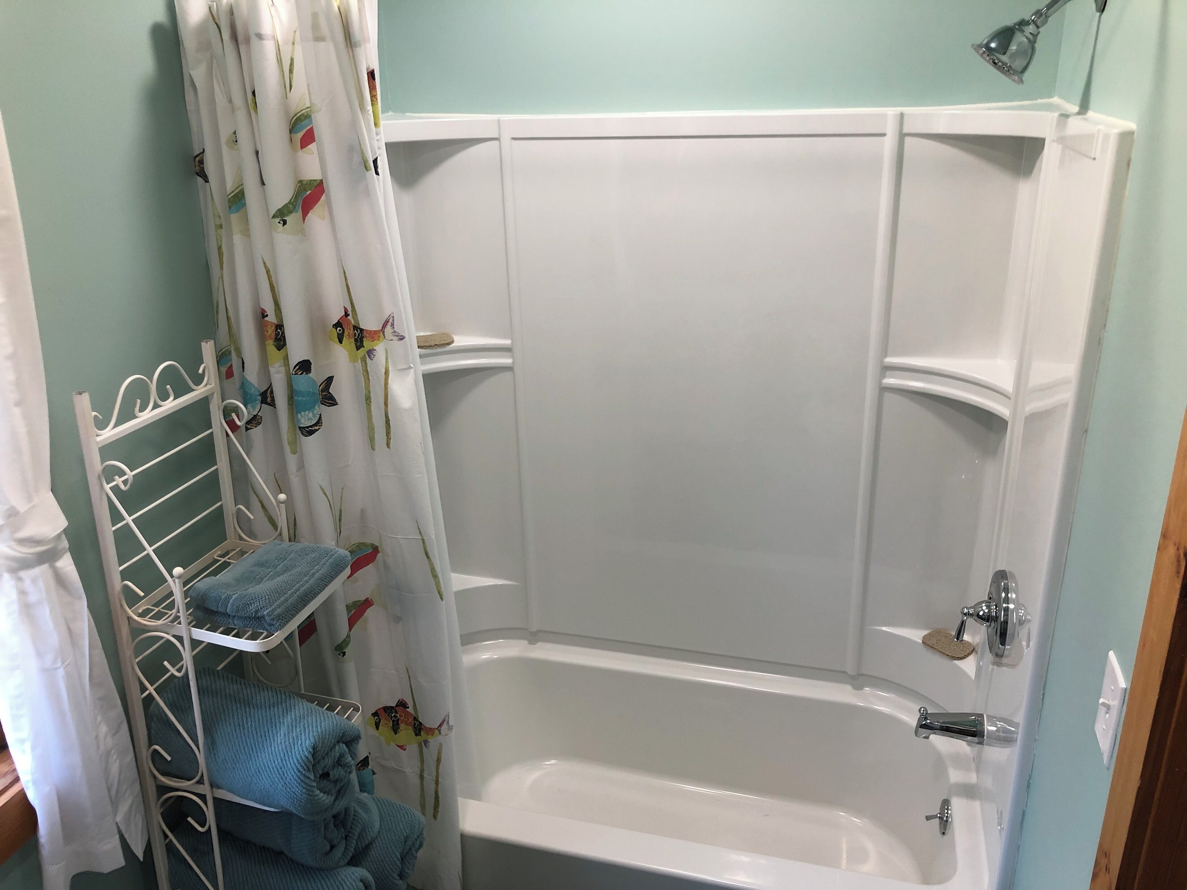 Une salle de bain avec une baignoire blanche, une étagère en métal avec des serviettes et un rideau de douche orné de motifs de poissons.