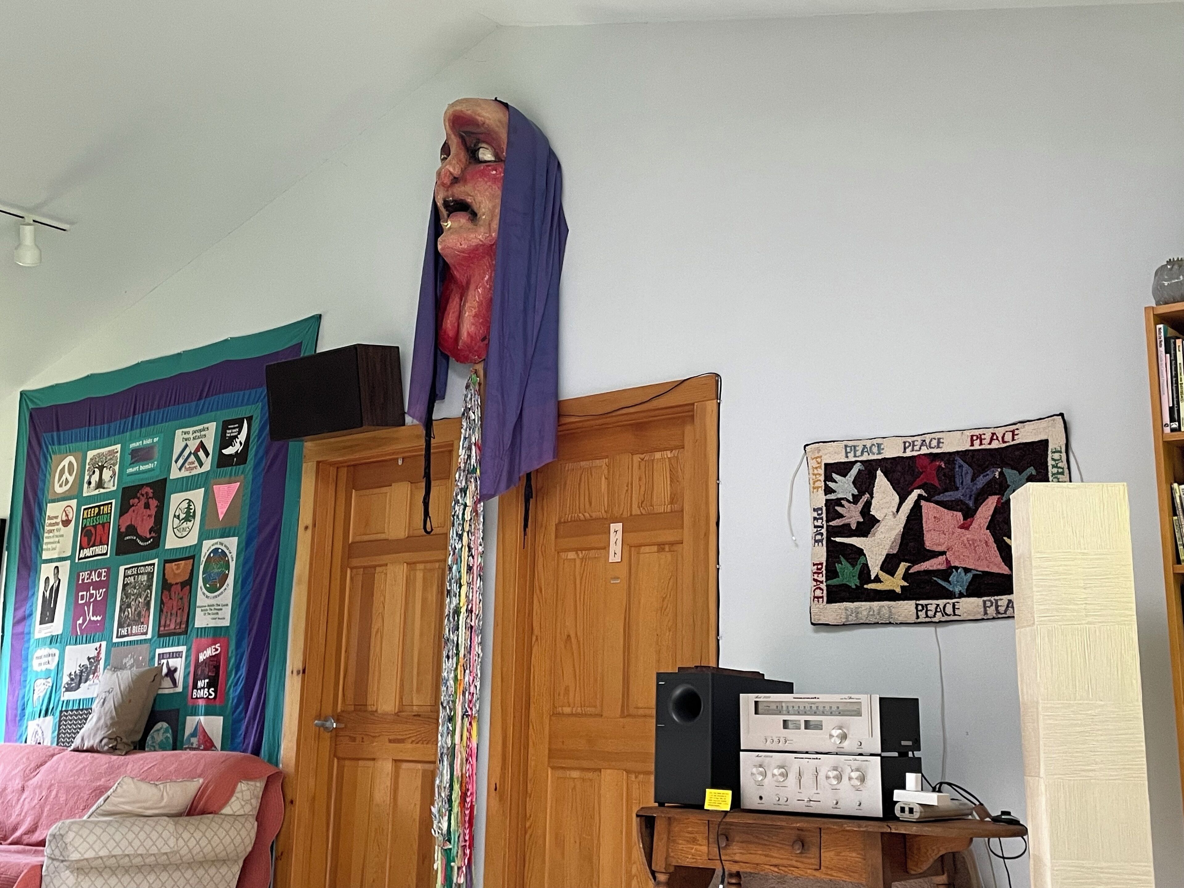 Una stanza con un armadio in legno, un copriletto con applicazioni a tema pace, un decoro murale a tema pace e un impianto stereo vintage.