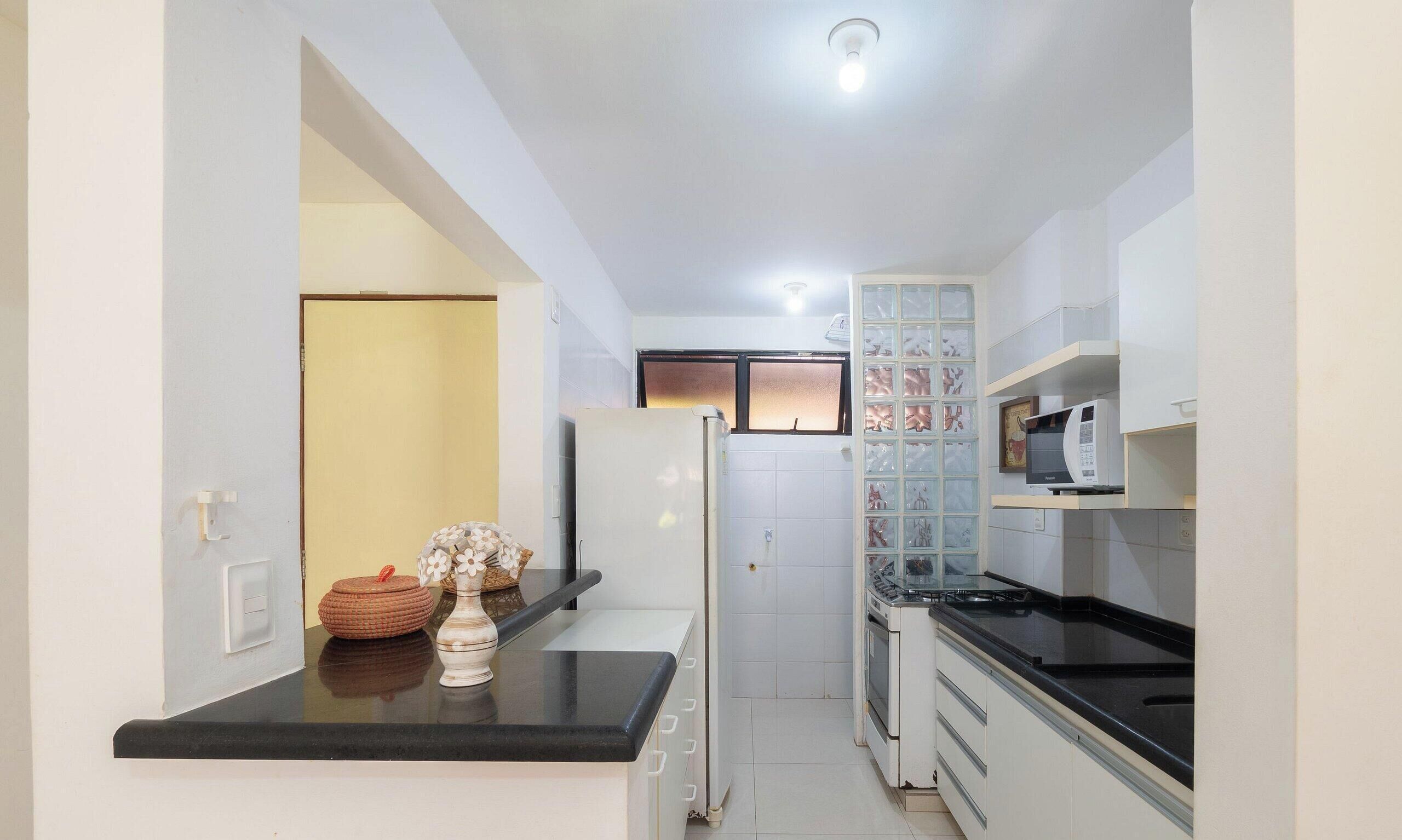 A compact kitchen with a black countertop, white cabinets, a microwave, and a window with frosted glass.
