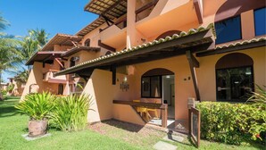 A multi-story building with a covered outdoor area, a pool, and lush greenery. - Condominium With Gym and Pool in Guarajuba - Camacari GSH (Camaçari)