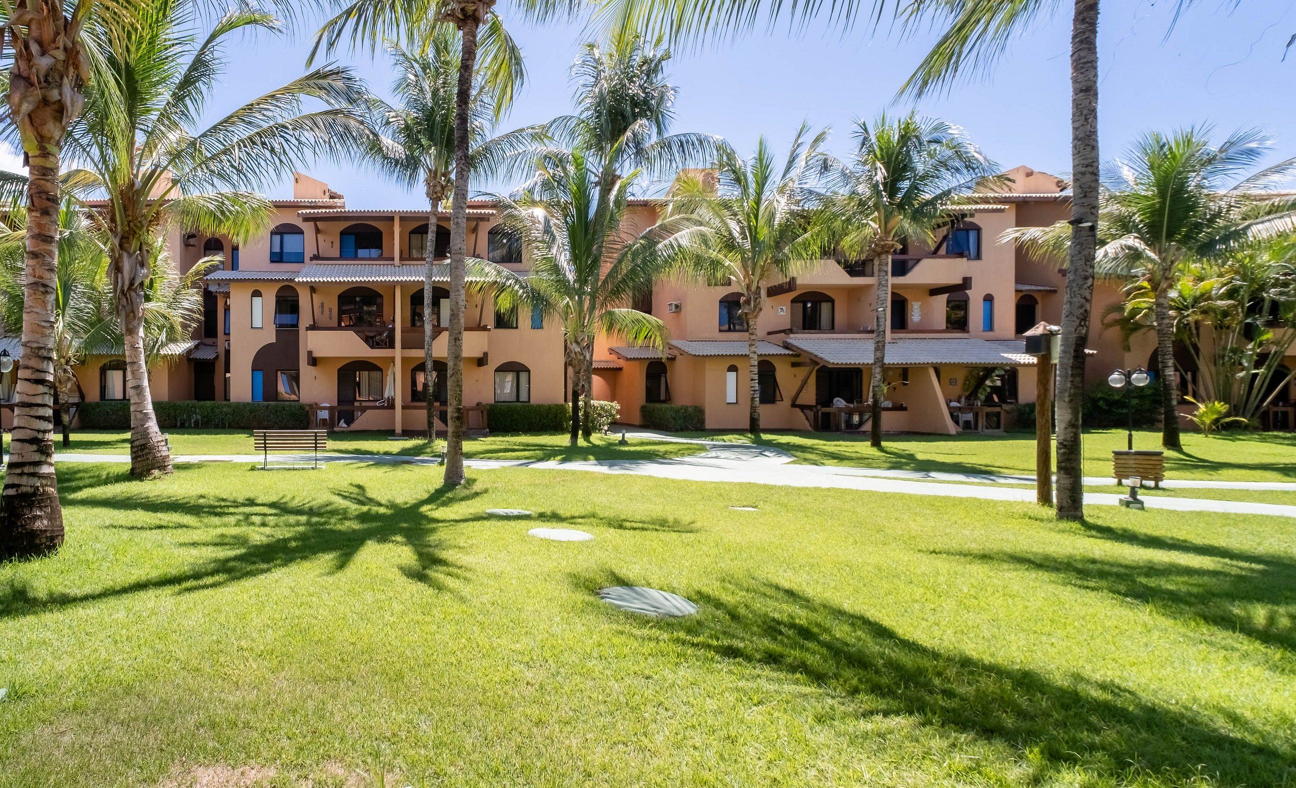 A hotel with multiple balconies, palm trees, and a well-maintained lawn.