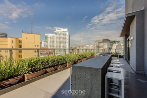 A rooftop terrace with a long, narrow seating area, a small water feature, and a view of surrounding high-rise buildings.