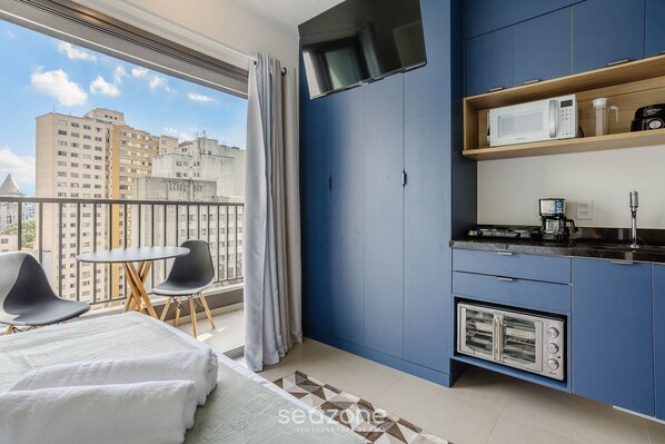 A modern kitchen with a built-in oven, a microwave, and a coffee maker. There is a balcony with a table and chairs, and a view of buildings outside.