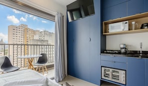 A modern kitchen with a built-in oven, a microwave, and a coffee maker. There is a balcony with a table and chairs, and a view of buildings outside. - Comfort w/ Balcony and View in Consolacao Vno1417 (São Paulo)