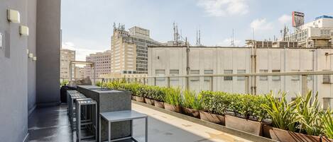 A rooftop terrace with a seating area, potted plants, and a view of surrounding buildings.