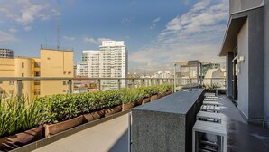 A rooftop terrace with a long, narrow seating area, a small water feature, and a view of surrounding high-rise buildings. - Studio w/ Balcony and View in Consolacao - Vno1417 (São Paulo)