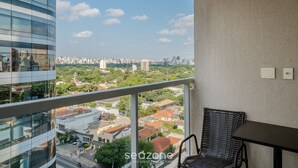 A balcony with a view of a cityscape, a wicker chair, and a table. - Modern Studio With Pool in Sao Paulo You1203 (São Paulo)