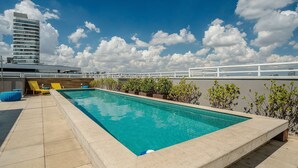A rooftop pool with a clear blue sky, a tall building in the background, and a white railing. - Modern Studio With Pool in Sao Paulo You1203 (São Paulo)
