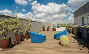 A rooftop terrace with potted plants, blue woven chairs, and a wooden floor. - Modern Studio With Pool in Sao Paulo You1203 (São Paulo)