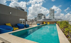 A rooftop pool with blue and yellow lounge chairs, a clear blue sky, and modern buildings in the background. - Modern Studio With Pool in Sao Paulo You1203 (São Paulo)