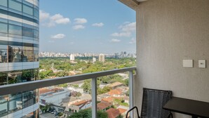 A balcony with a view of a cityscape, a wicker chair, and a table.