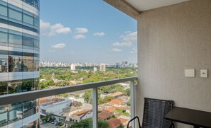 A balcony with a view of a cityscape, a wicker chair, and a table. - Modern Studio With Pool in Sao Paulo You1203 (São Paulo)