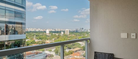 Un balcon donnant sur un paysage urbain, une chaise en osier et une table.