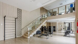 A spacious gym with a staircase, exercise equipment, and a large mirror. - Studio in Condominium With Pool in Paraiso Zah0811 (São Paulo)