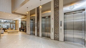 A modern lobby with a clean, polished floor, a seating area with sofas, and two elevators with a decorative wall panel. - Studio in Condominium With Pool in Paraiso Zah0811 (São Paulo)