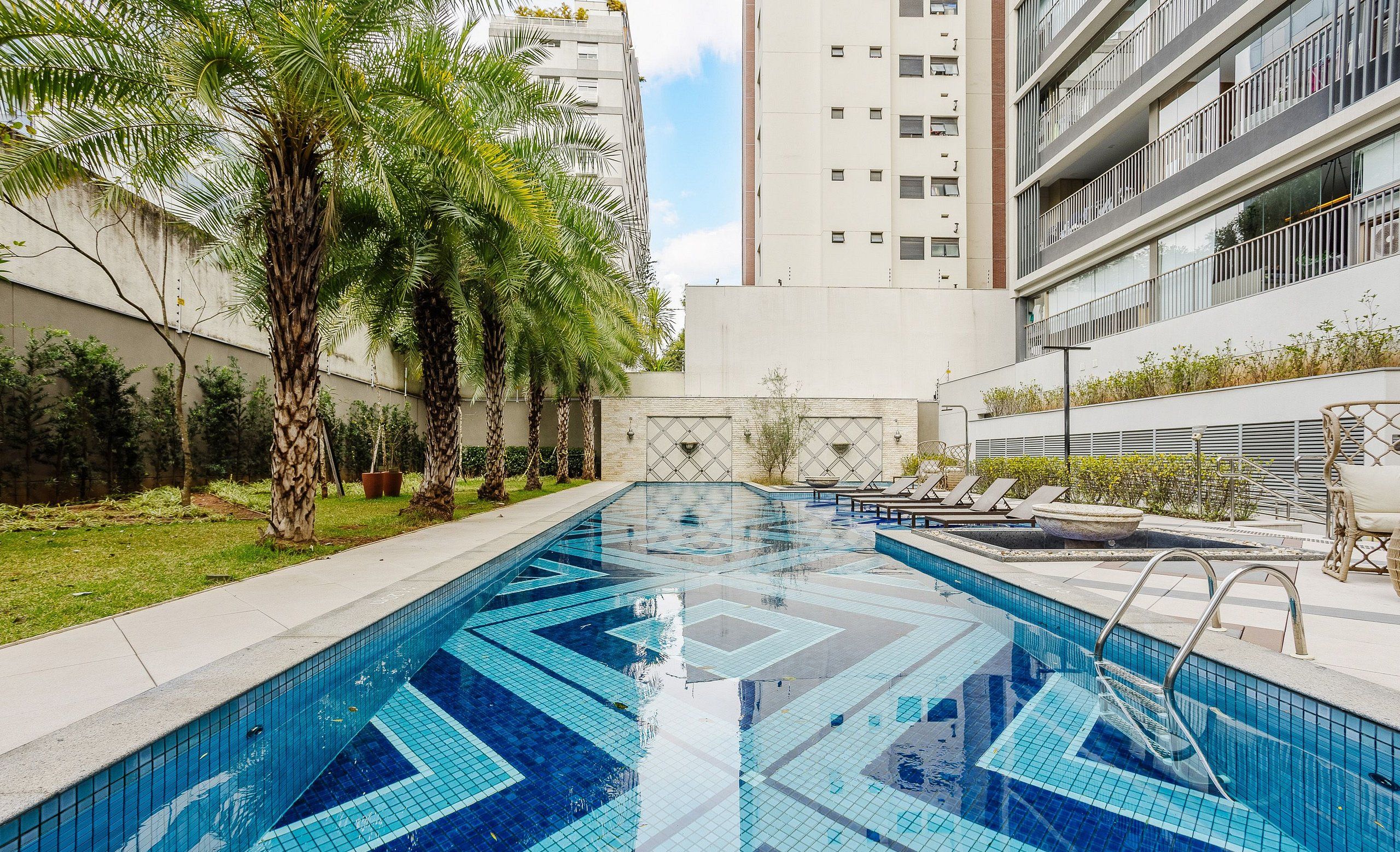 A swimming pool with geometric tile patterns, surrounded by palm trees and lounge chairs, with modern buildings in the background.