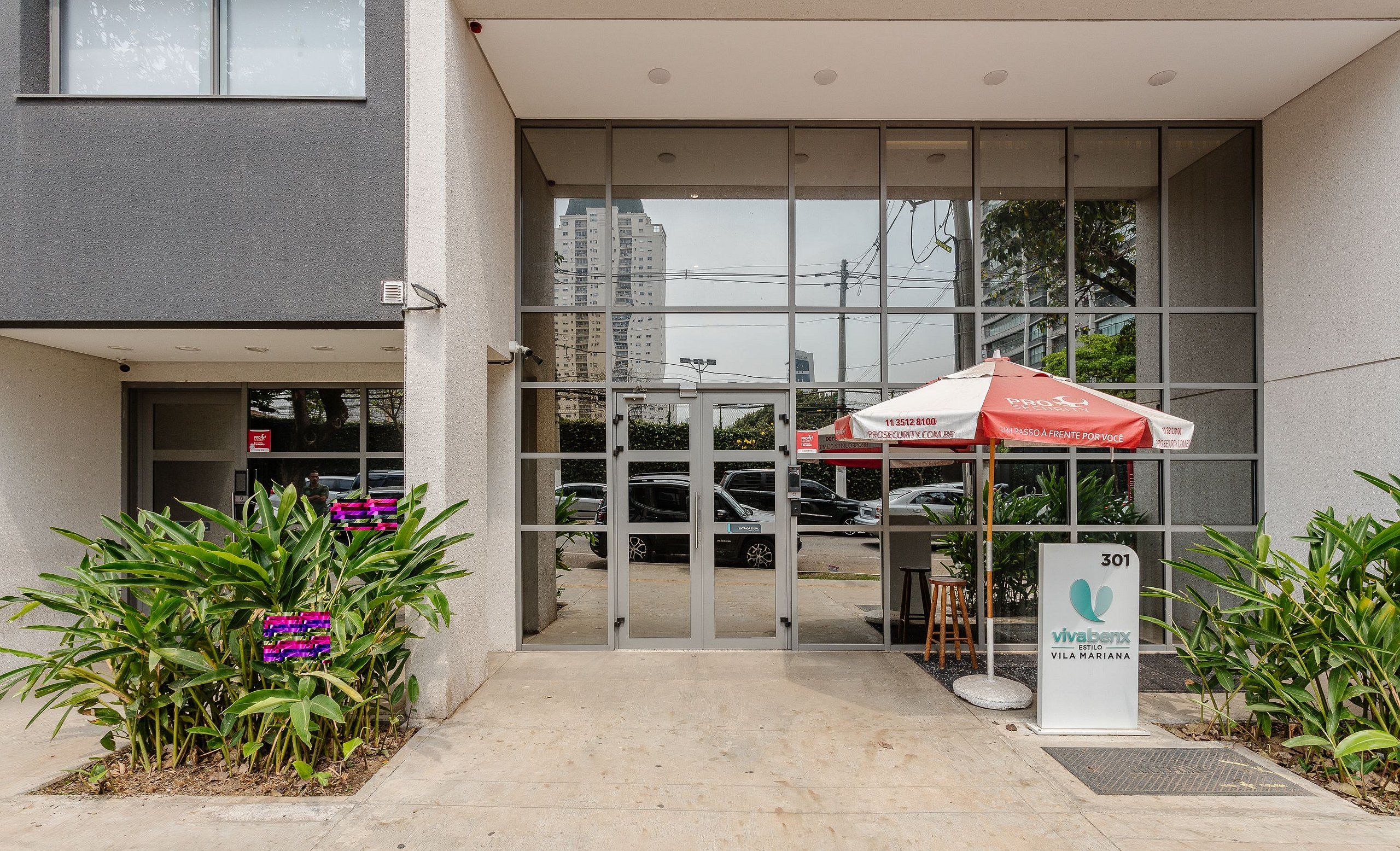 A building entrance with a glass door, a red and white umbrella, and a sign with a phone number.