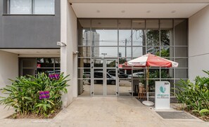 A building entrance with a glass door, a red and white umbrella, and a sign with a phone number.