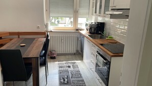 A compact kitchen with a dining area, featuring a built-in oven, a coffee machine, and a window with blinds. - WatzmannEG (Augsburg)