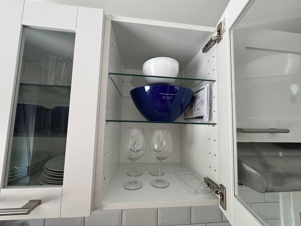 A kitchen cabinet with a glass shelf holding a blue bowl and two wine glasses.