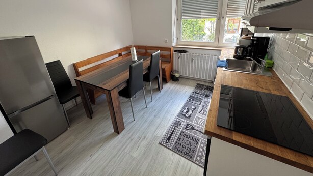 A compact kitchen with a dining table, chairs, a refrigerator, and a window with blinds. - WatzmannEG (Augsburg)