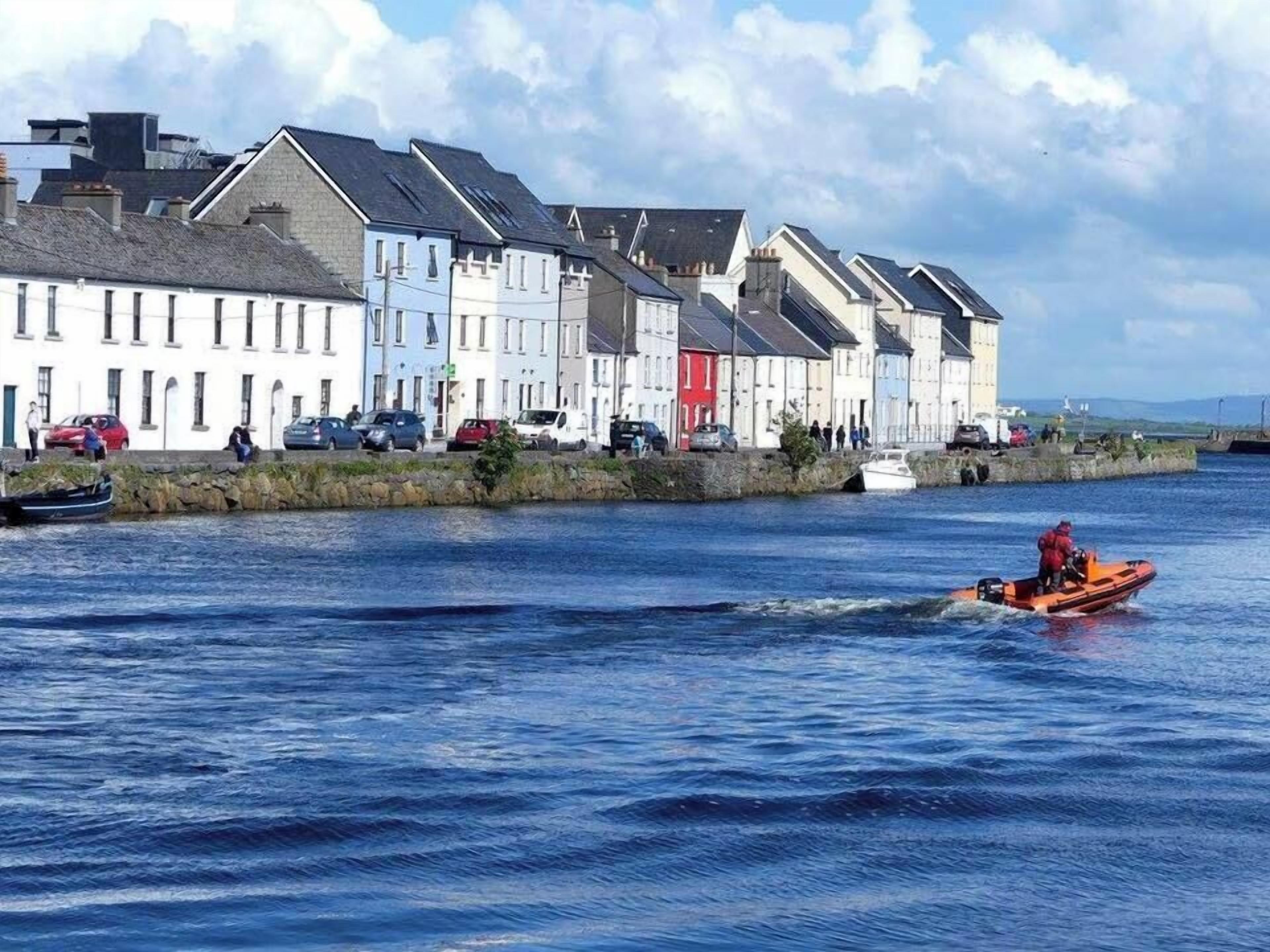 A waterfront with colorful buildings, a boat on the water, and a stone wall.