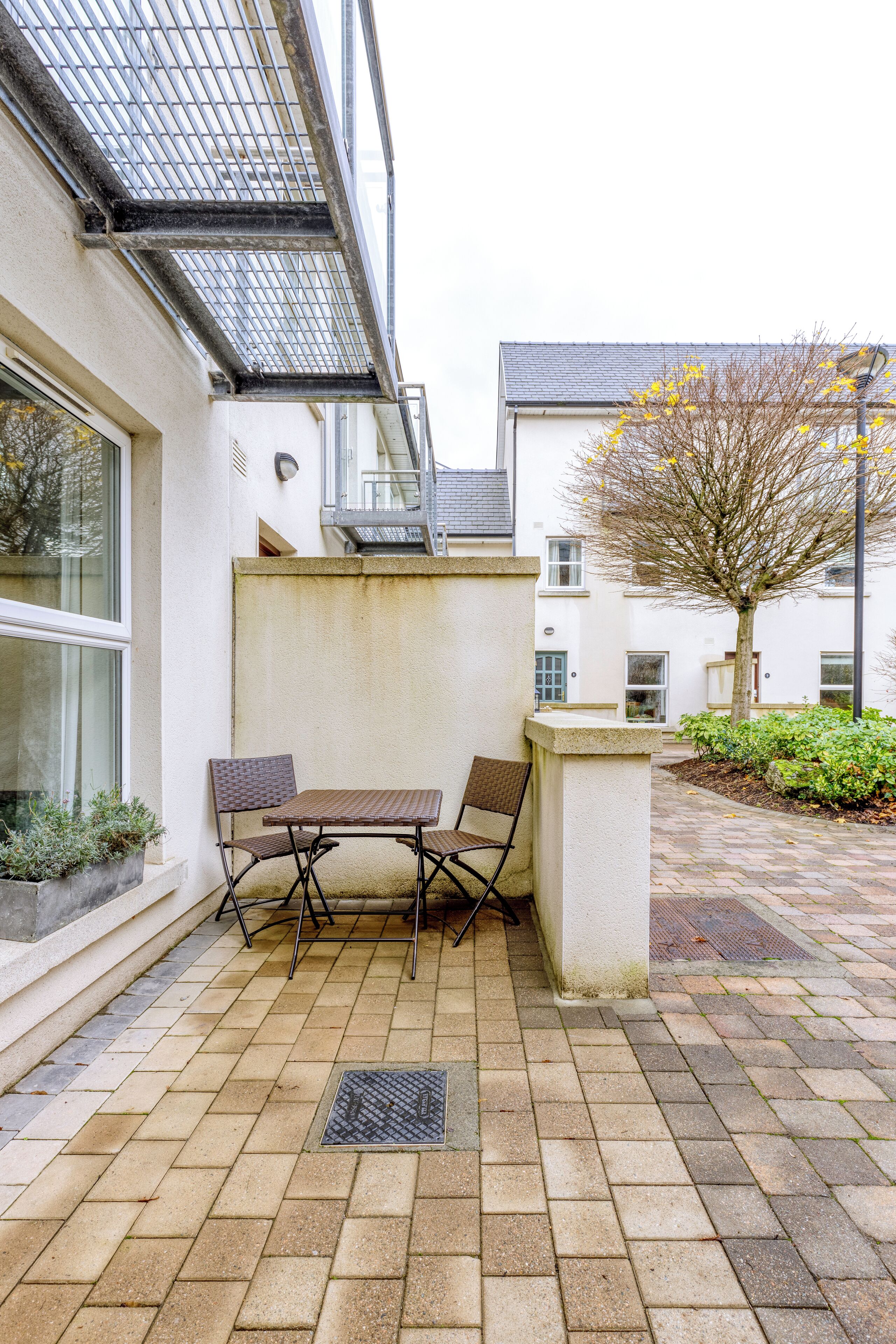 A patio with a table and chairs, a potted plant, and a tree.