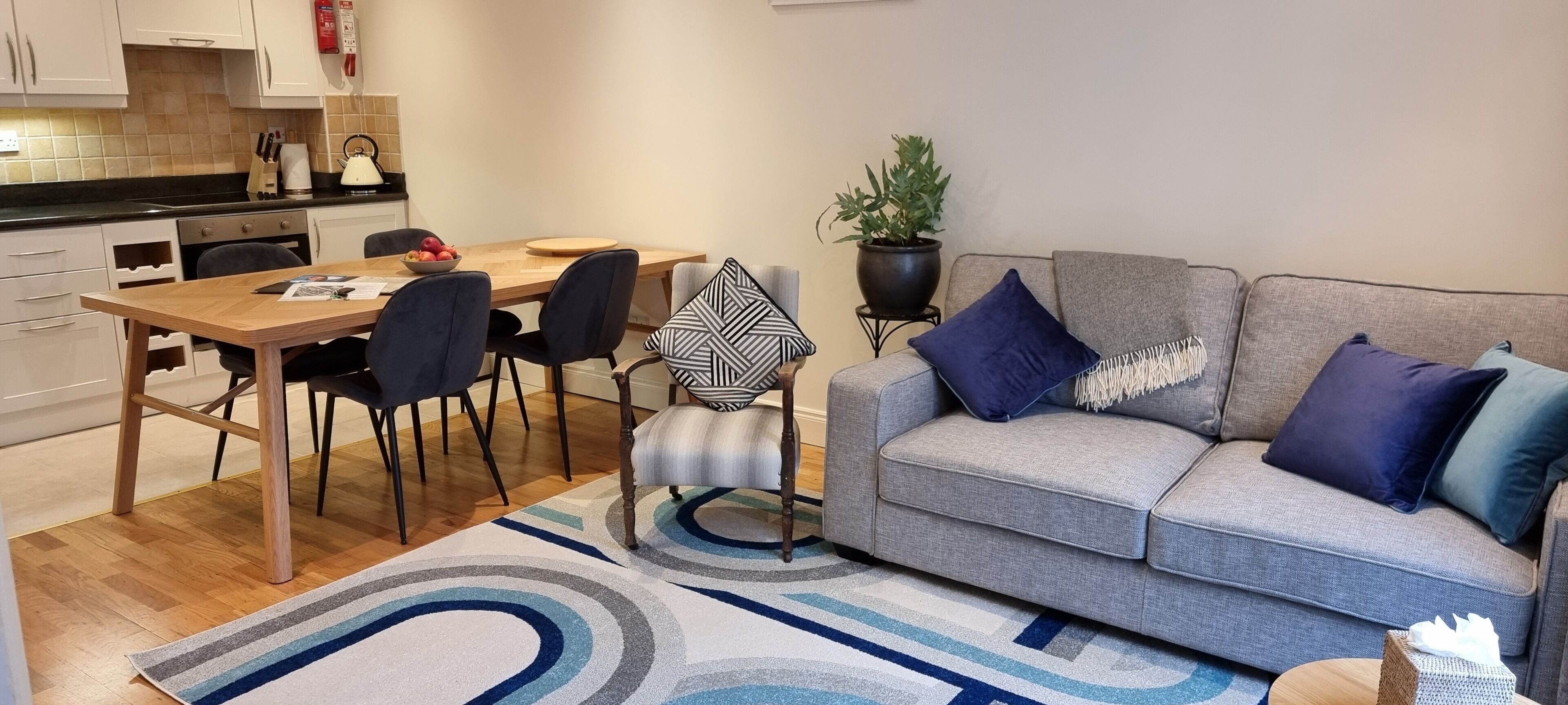 A modern living room with a grey sofa, blue and white patterned rug, and a dining area with a wooden table and chairs.