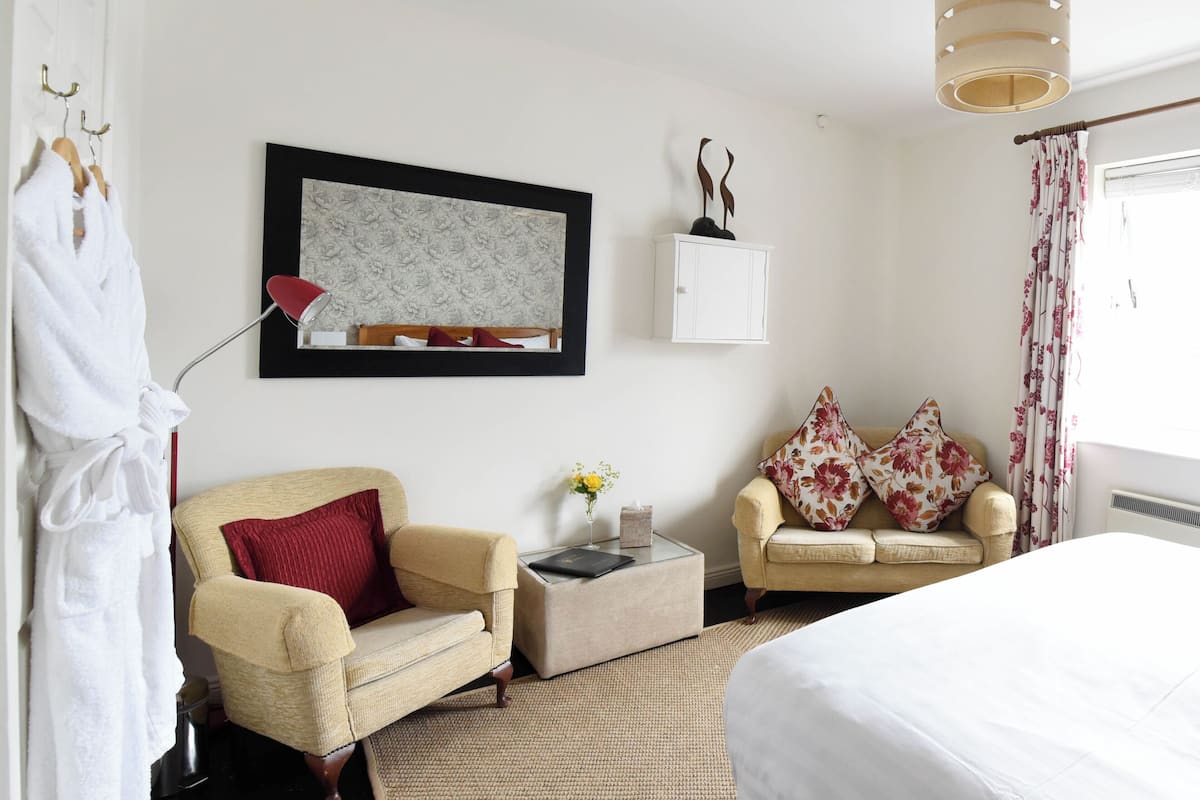 A hotel room with a bed, two armchairs, a small table, a framed picture on the wall, a cabinet, and a window with curtains.