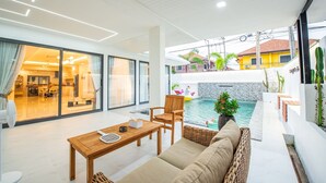 A modern living room with a pool, a dining area, and a view of a yellow house.