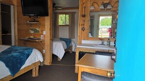 A wooden cabin with two beds, a television, a sink, and a mirror.